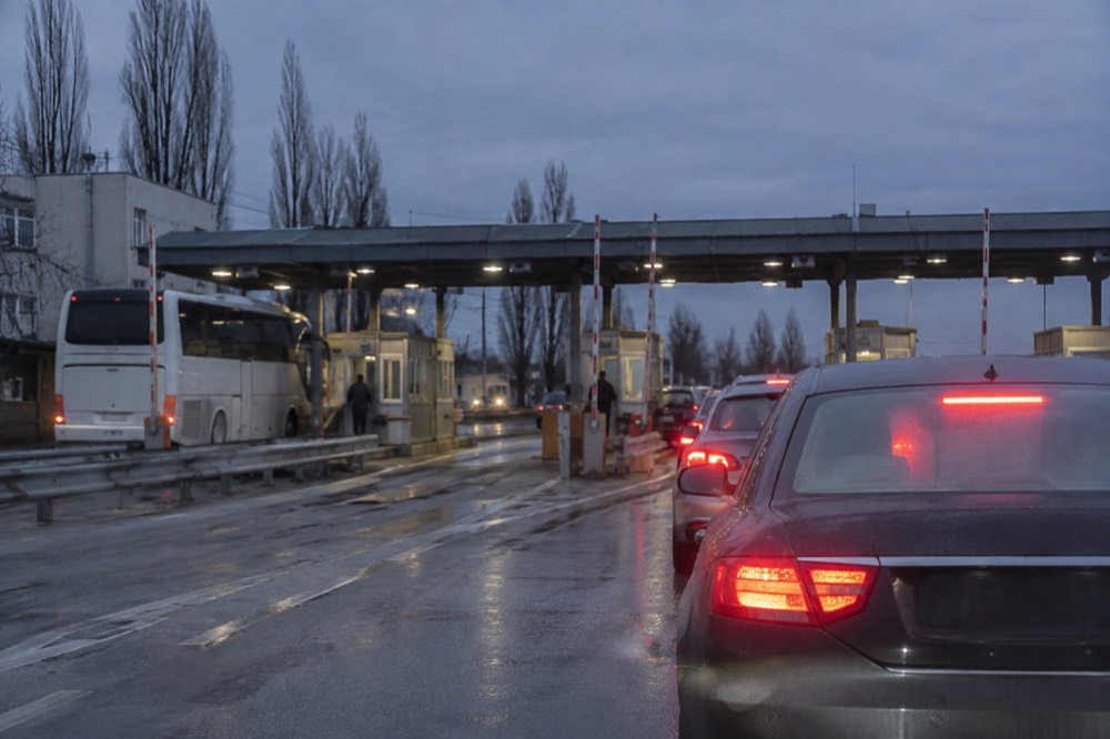 A border crossing checkpoint with a sign in multiple languages, and a tour bus in a separate lane.