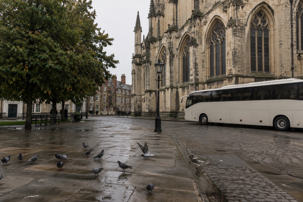 A comfortable touring coach parked outside a historic stone cathedral in a European city square