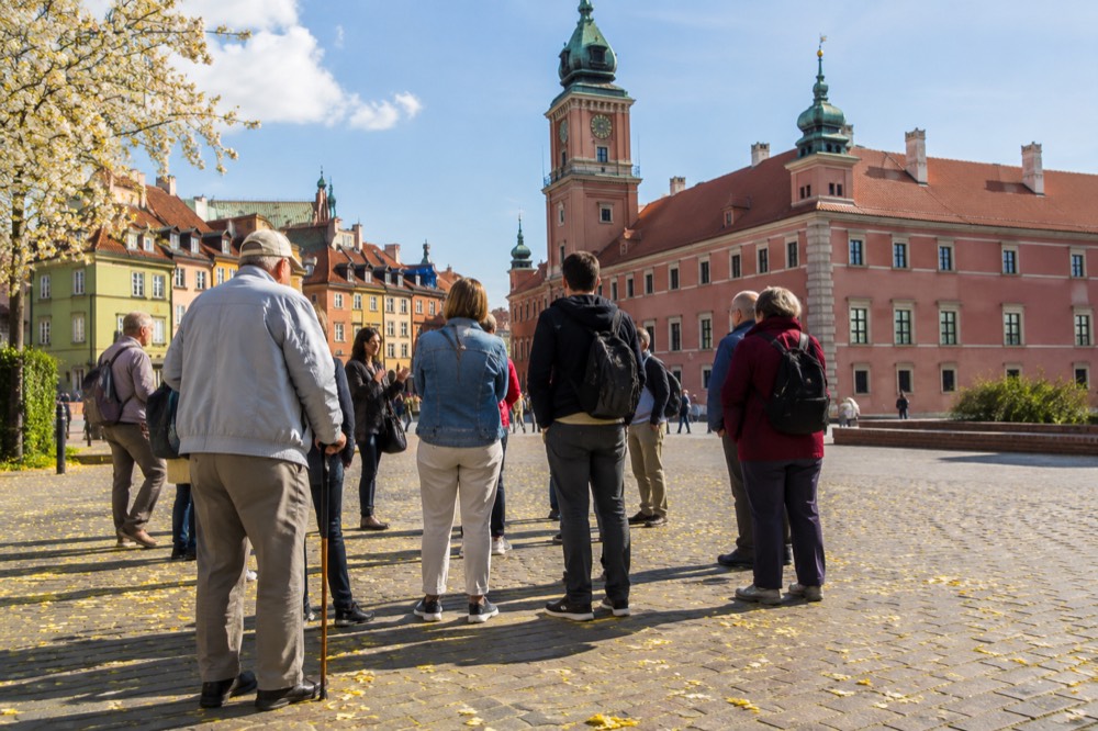 A small group of travellers gathered around a guide in front of a historic European palace facade