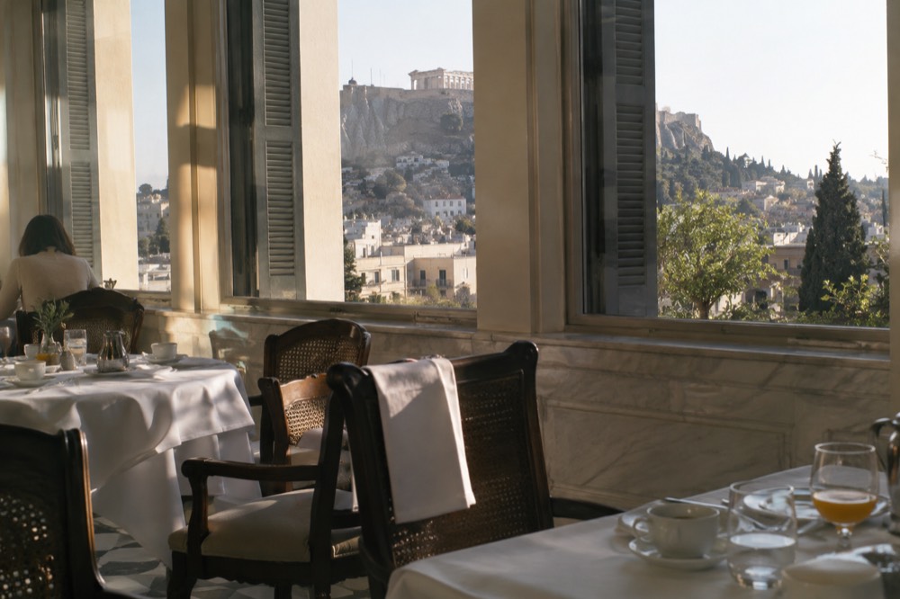 A hotel dining room with tables set for breakfast beside tall windows