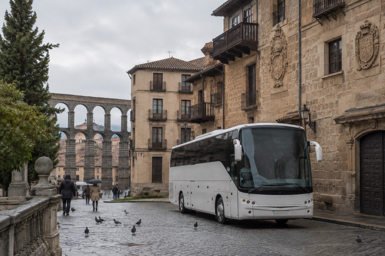 A touring coach parked on a cobbled street beside old European stone buildings