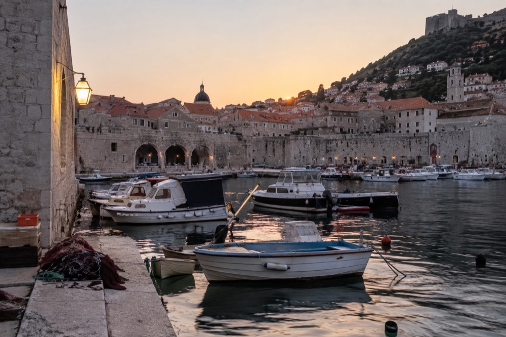 Coastal European town at dawn with pastel buildings along a calm harbor