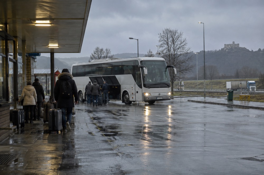 Long-distance coach parked at a rest stop on a European highway with passengers waiting beside luggage