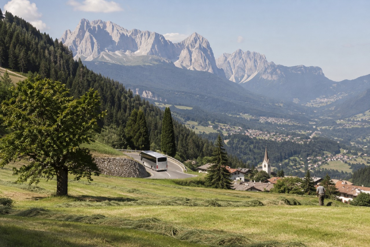 A coach parked on a mountain road above an alpine valley with villages in the distance
