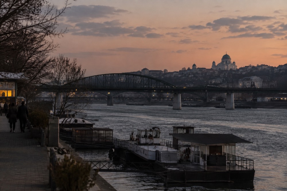 Riverside city skyline with a Gothic cathedral and an arched stone bridge at dusk
