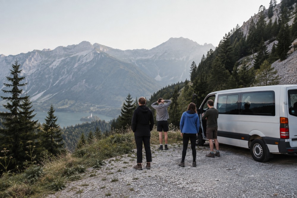 A small minibus parked on a mountain road with a few travelers stretching outside