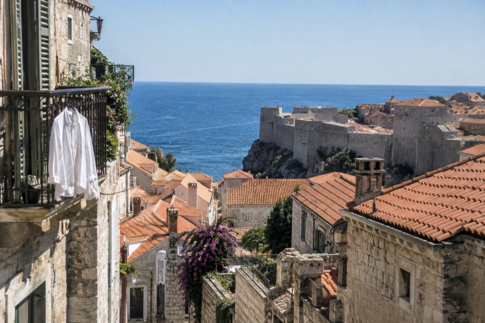 Walled old town buildings climbing a hillside above a blue Adriatic bay
