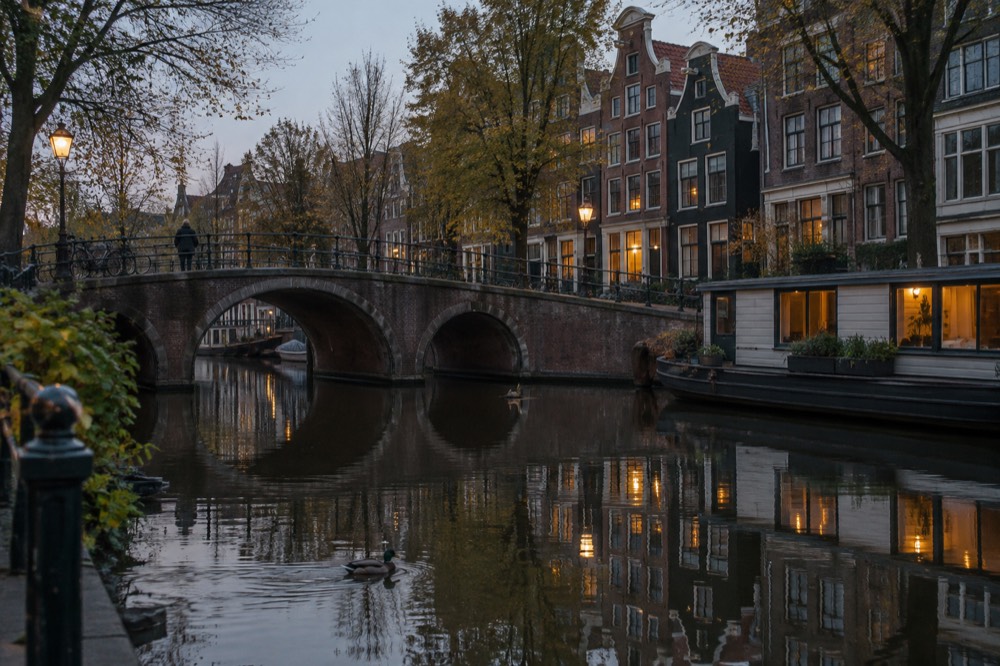 Colourful canal houses reflected in the still water of an Amsterdam canal with bicycles parked on the bridge