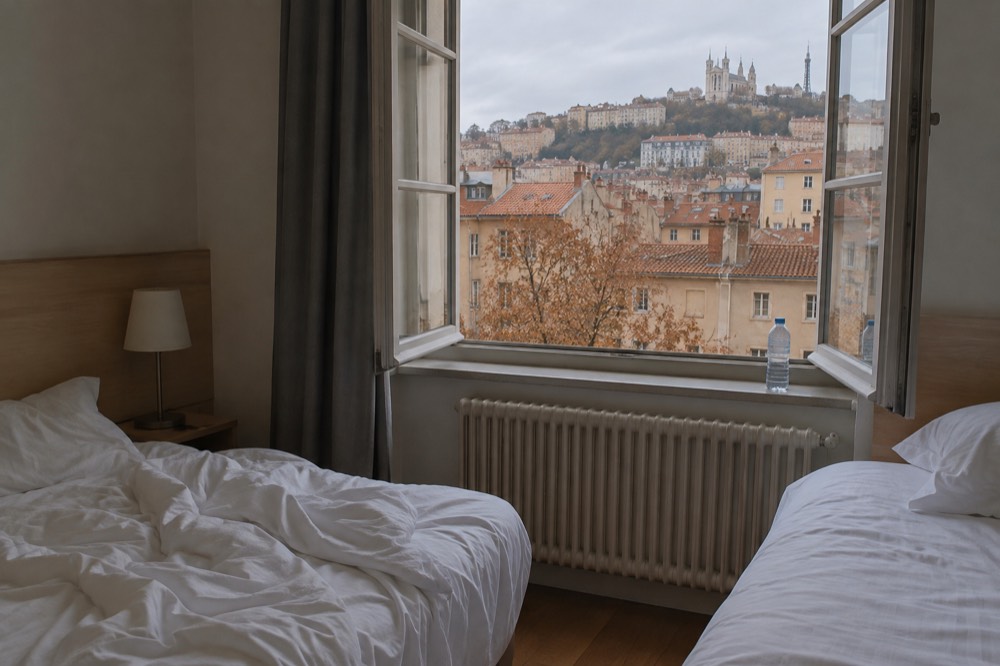A simple twin hotel room in Europe with a city view through an open window