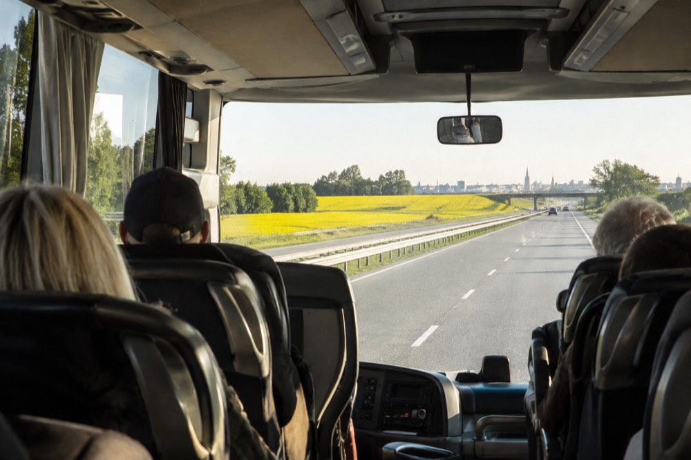 A tour coach driving on a highway past a road sign listing several European cities