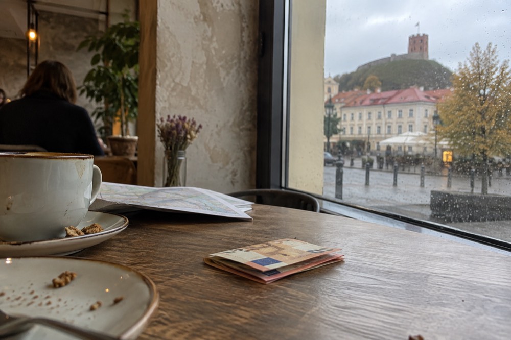 A traveller counting euro banknotes beside a trip itinerary on a cafe table