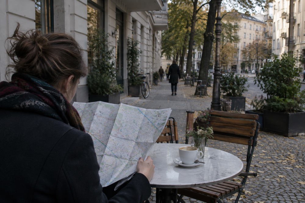 A traveller reading a paper map at a cafe table on a European street
