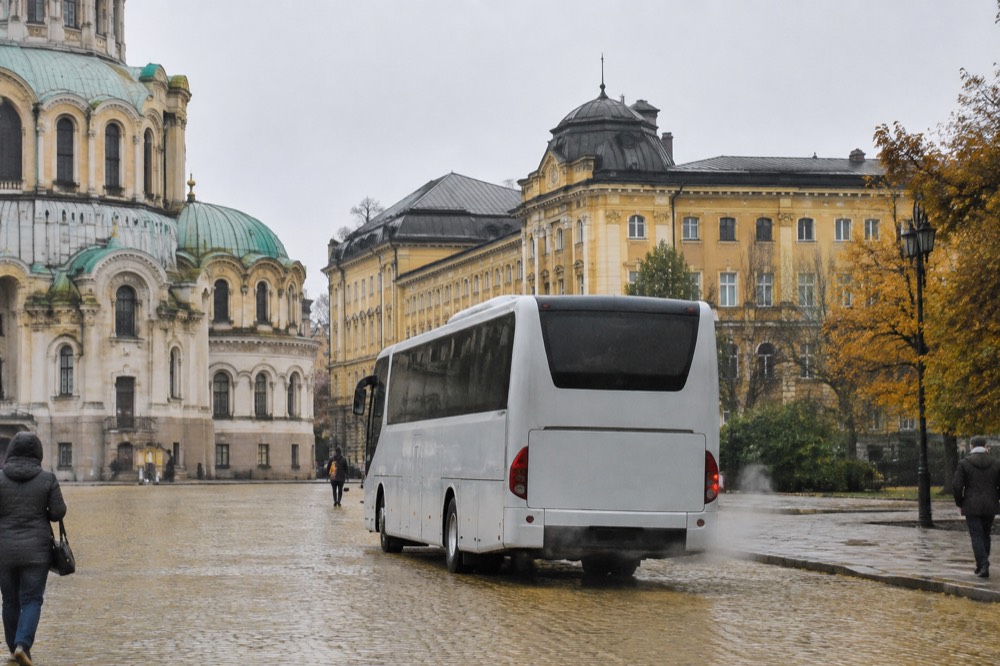 A tour coach parked on a cobblestone square in front of old European buildings