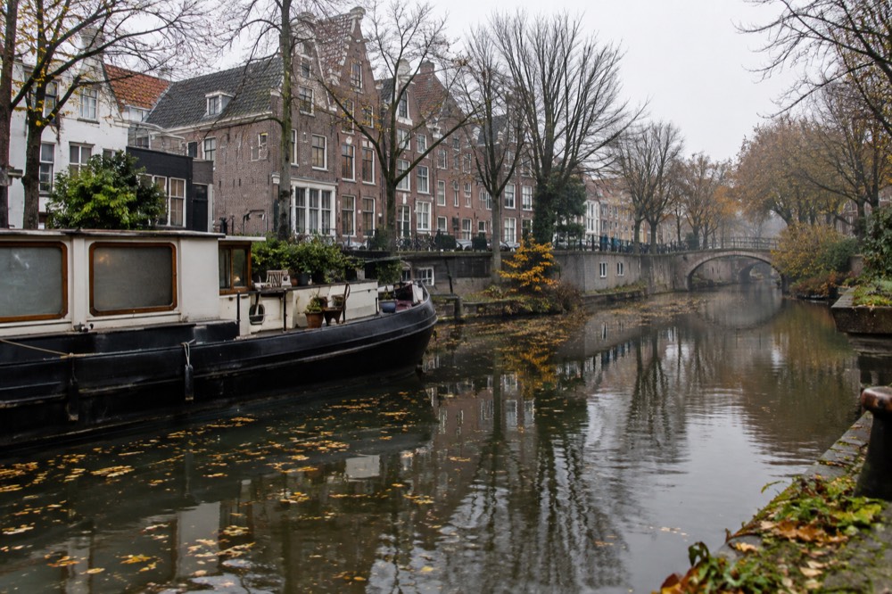 A canal in a European city lined with autumn trees and old gabled houses reflected in still water