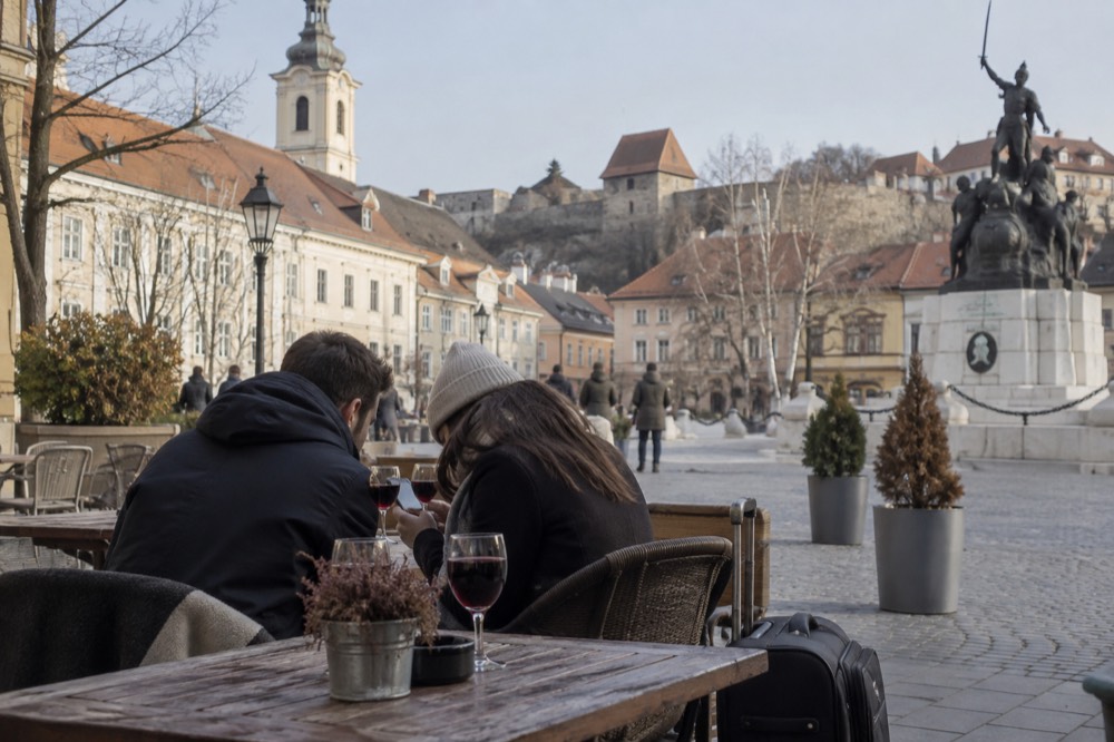 A couple checking a phone at a cafe table with luggage leaning against the chair