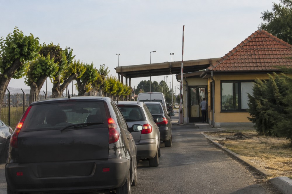 A border control booth at a road crossing between two European countries with a queue of vehicles