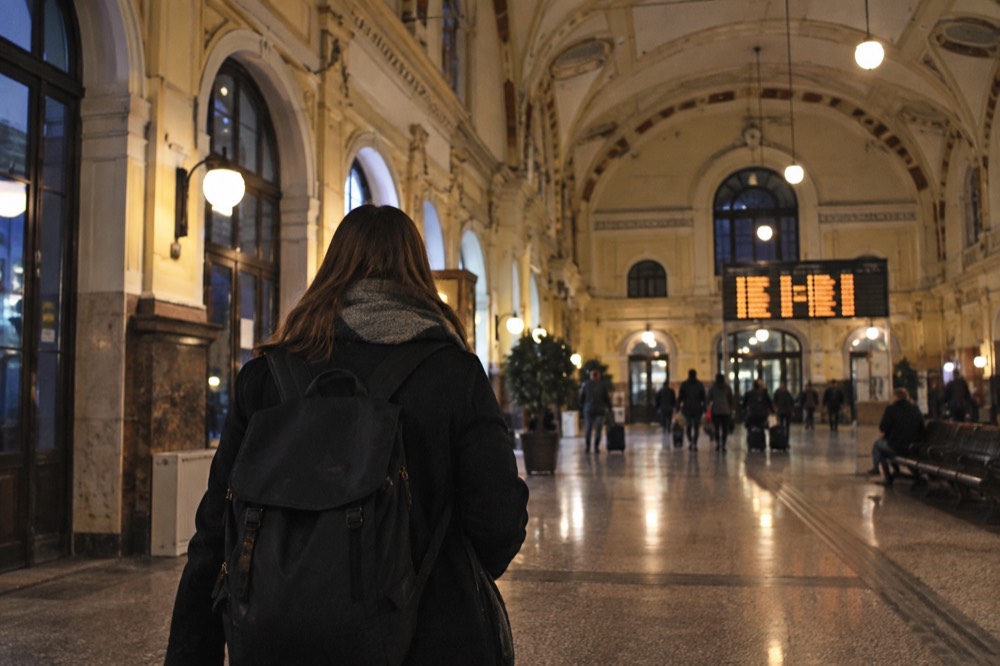 A traveller with a backpack watching a departure board in a vaulted European station concourse