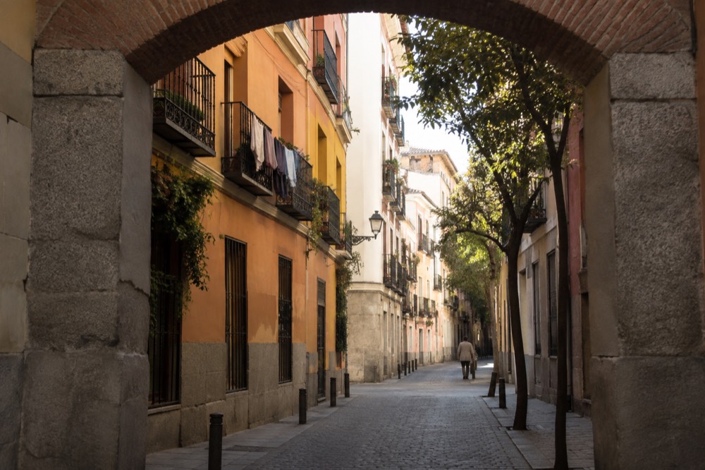 A European old town street with pastel buildings and a stone archway in morning light