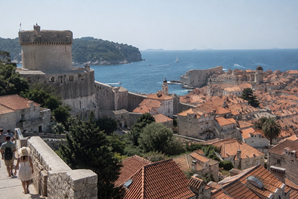 A walled old town beside blue sea with red rooftops and a stone fortification