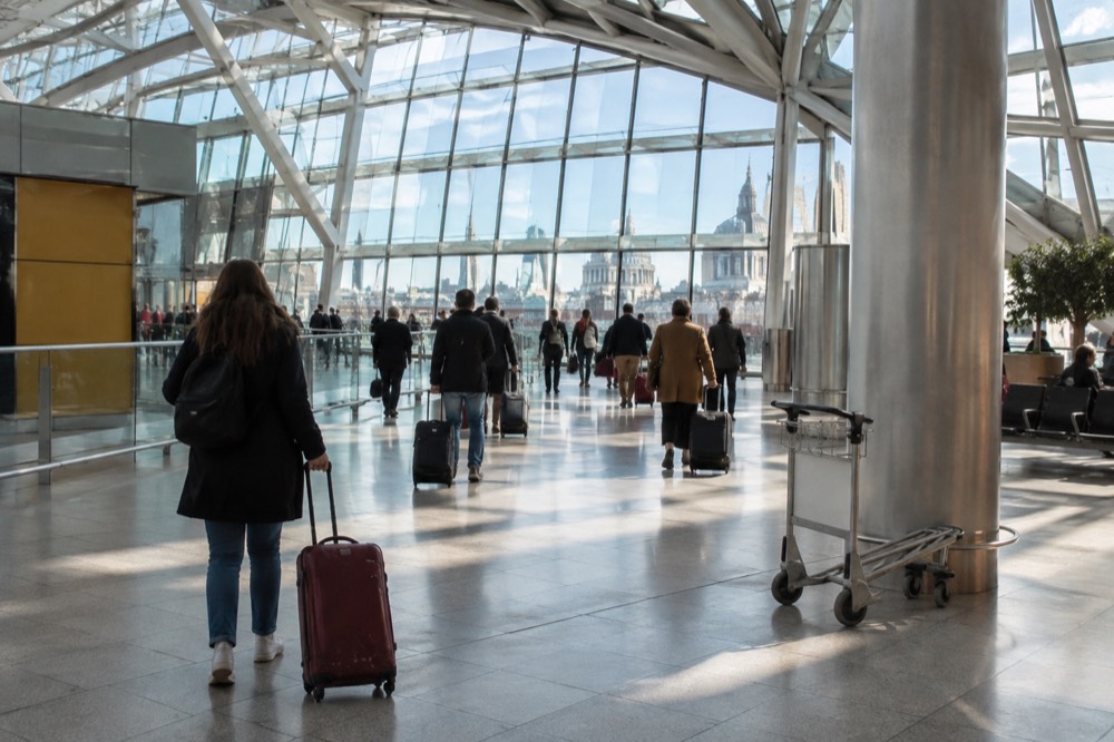 Travellers with suitcases crossing a bright airport terminal concourse under a high glass roof