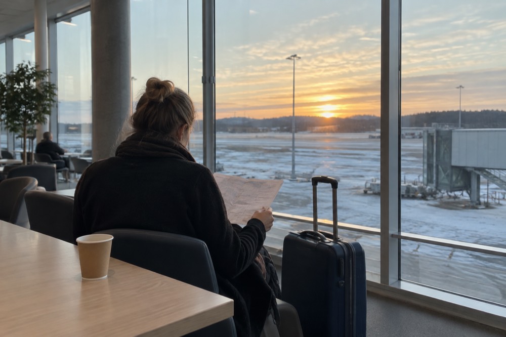 Traveller checking a paper itinerary beside a suitcase in a bright airport lounge