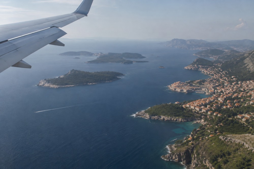 Airplane wing above a coastline with islands scattered across blue water
