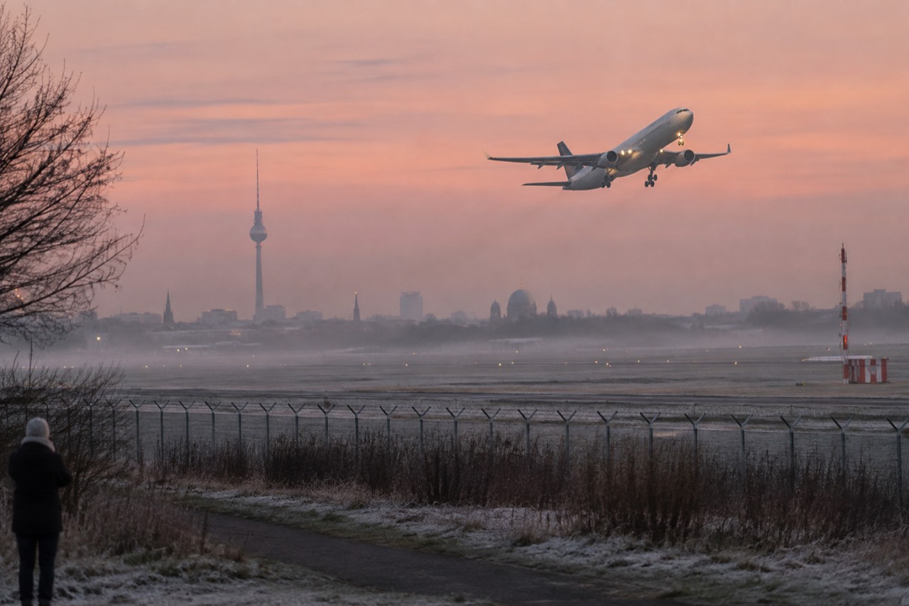 A wide-body airliner climbing above a runway toward open sky at dawn