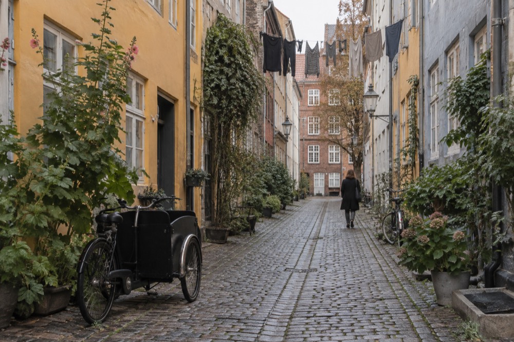 A narrow old town street in a European capital with pastel facades and a stone pavement