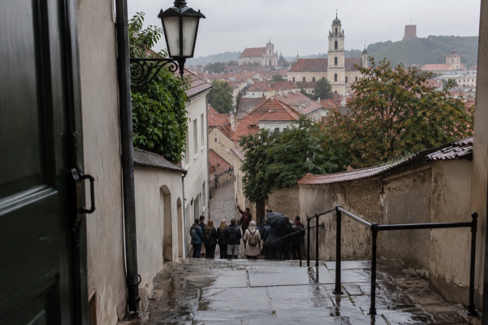A local guide speaking to a small group gathered on stone steps in a European old town