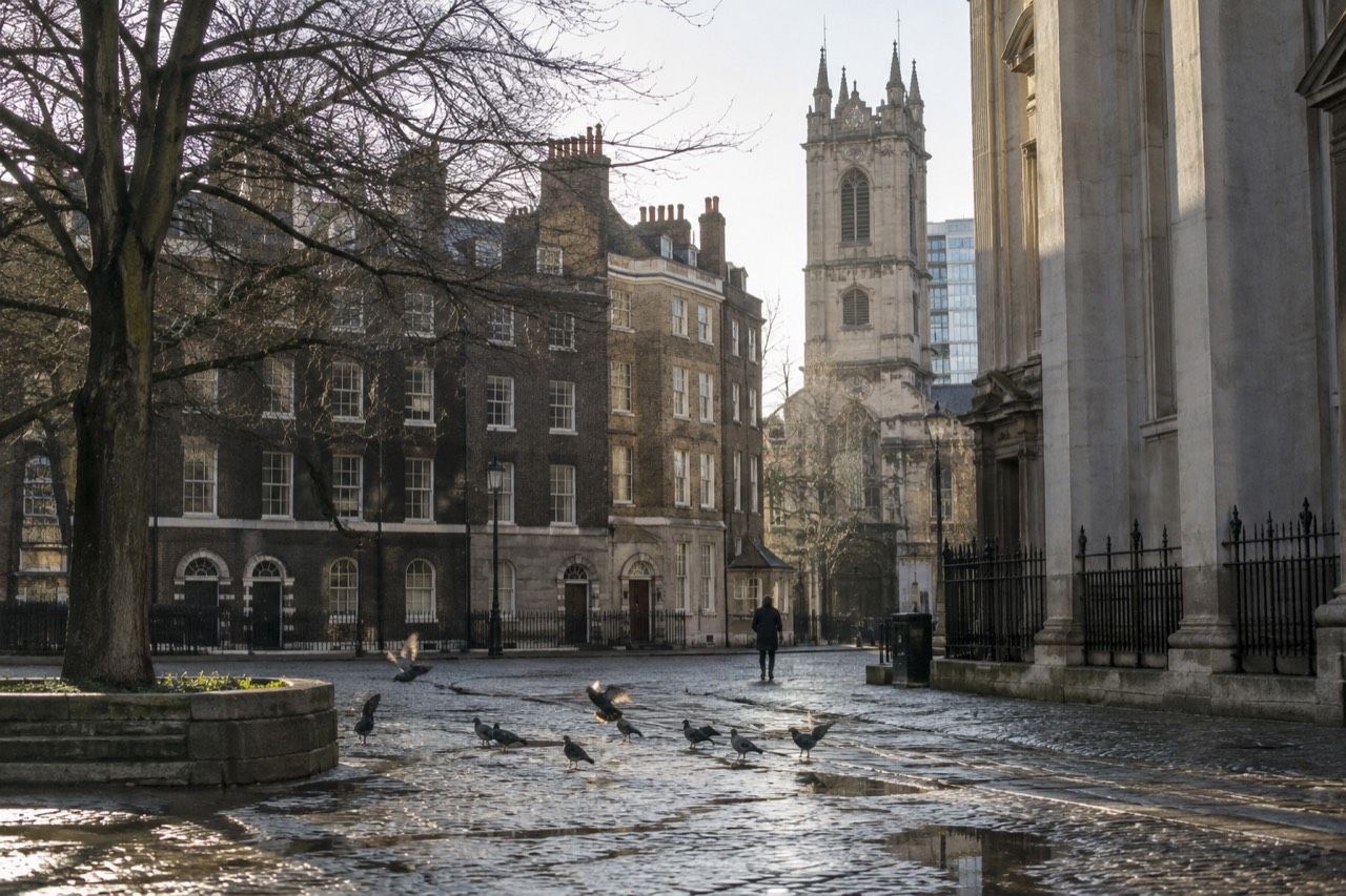 A cobbled European square at morning with old town rooftops and an empty lane