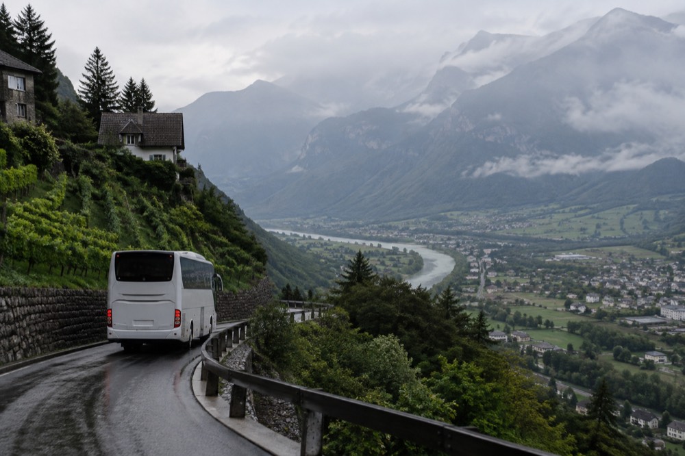 A tour coach on a mountain road above a river valley in the Alps