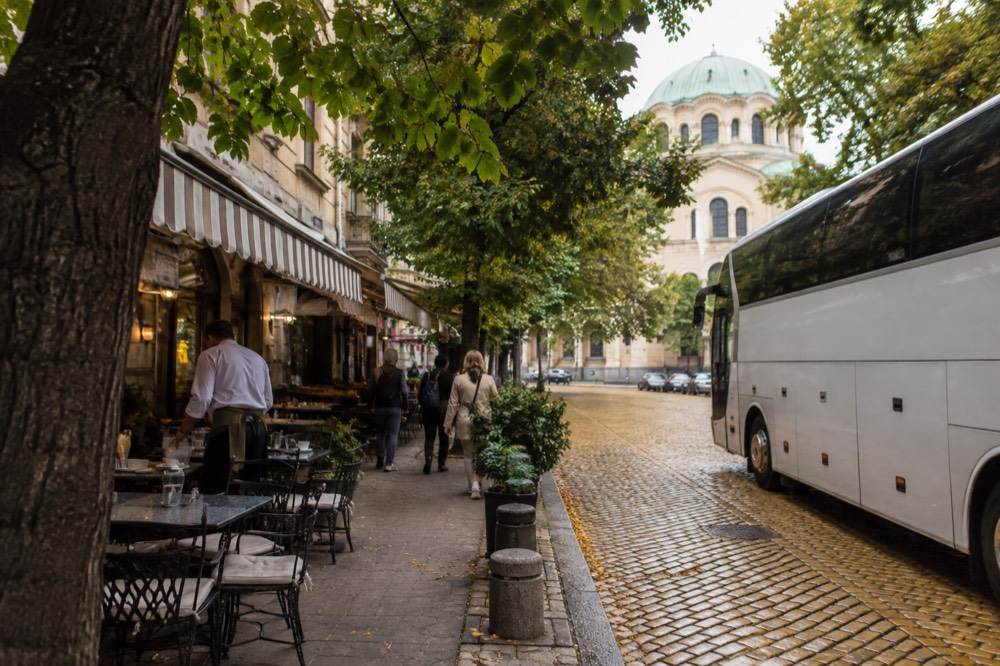 A tour coach parked outside a row of European cafes with awnings