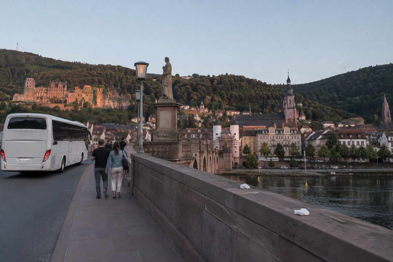 A coach parked on a European street beside a stone bridge and old town buildings