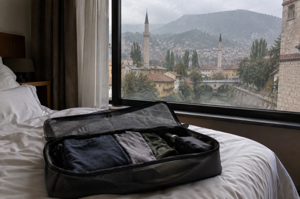 A packing cube opened on a hotel bed showing folded shirts and a small toiletry bag