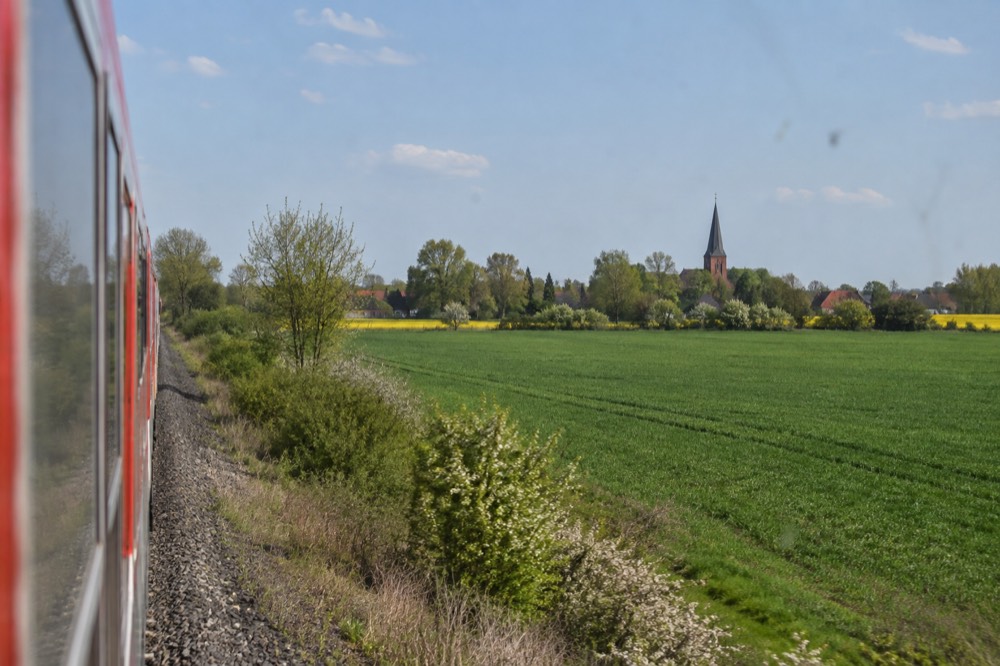 A long-distance train passing through green countryside with a village church in the distance