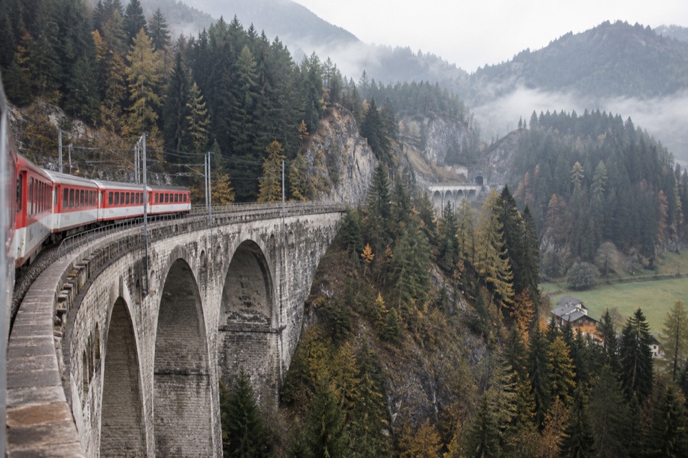 A scenic train crossing a stone viaduct above an Alpine valley