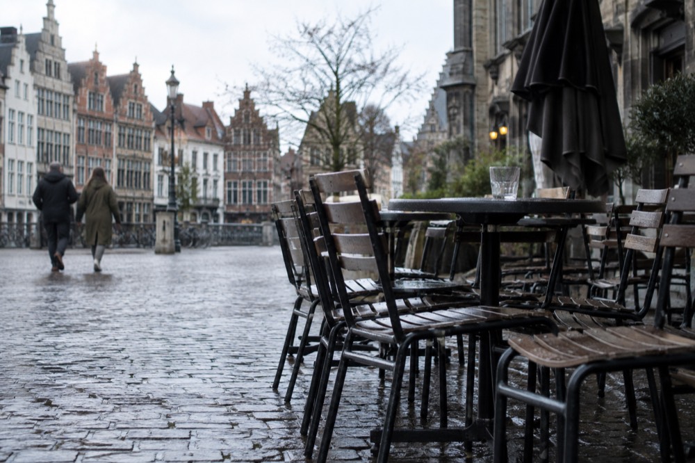 A quiet European old town square in early morning light with cafe tables set out