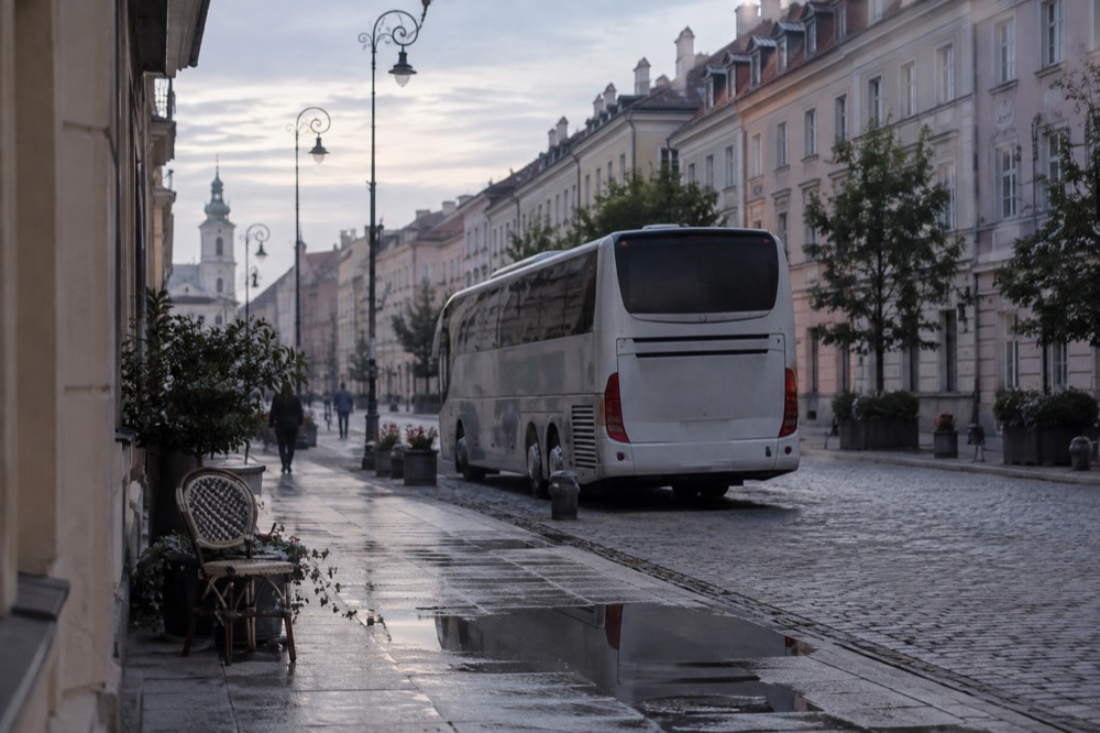 A tour coach parked on a cobbled street beside old European buildings in early morning light
