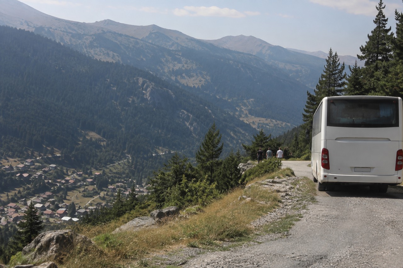A coach parked on a mountain road above an Alpine valley with village rooftops below