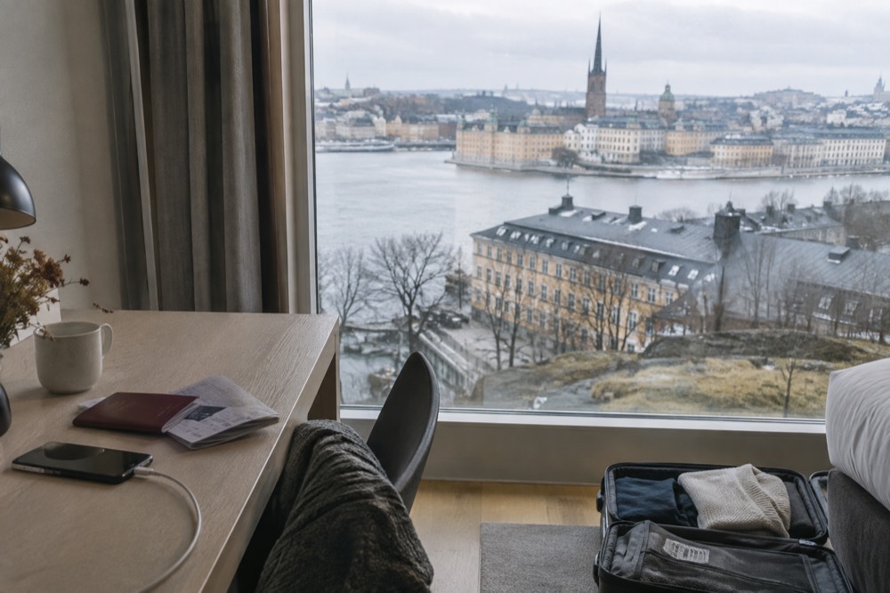 A passport and travel documents on a hotel desk beside a suitcase